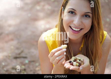 Ragazza sorridente sana che mangia un mix di frutta secca di semi di noci guardando la macchina fotografica. Spazio di copia. Foto Stock