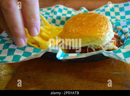 La persona sta mangiando un hamburger di carne e patatine fritte. Foto Stock