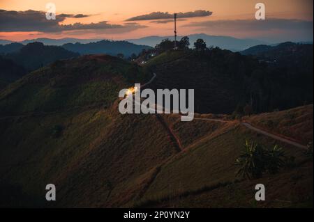 Auto leggera che guida su strada sterrata lungo la collina in cima al tramonto in altopiano rurale Foto Stock