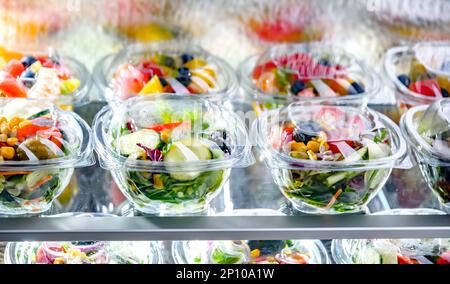 Scatole di plastica con insalate di frutta e verdura preconfezionate, messe in vendita in un frigorifero commerciale Foto Stock