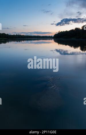 Massi subacquei nel fiume al crepuscolo, paesaggio del fiume Sava con silhouette foresta sulla riva e nuvole che si riflettono in acqua Foto Stock