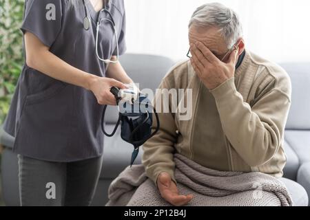 Giovane infermiera sorridente che prende la pressione sanguigna del vecchio Foto Stock