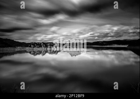Foto in bianco e nero ad alto contrasto di un lago perfettamente calmo in una lunga esposizione con riflessi. Foto Stock