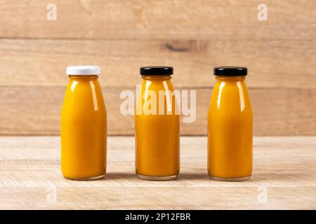 Tre frullati di ananas per mangiare sano in bottiglie di vetro su uno sfondo di legno. Concetto di nutrizione sana, disintossicante e dietetica. Foto Stock