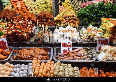 Molti spuntini e frutti di mare nel mercato notturno vietnamita con segni con testo vietnamita 'tempo, prezzo' traduzione Foto Stock