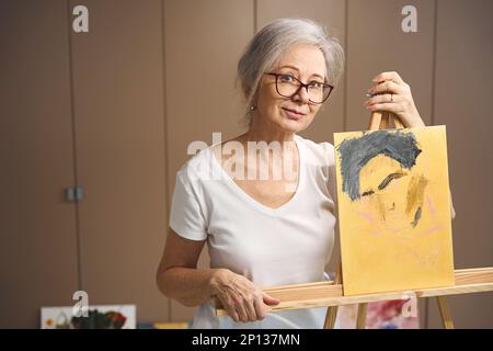 Il pensionato anziano è in piedi su un cavalletto con un ritratto incompiuto Foto Stock