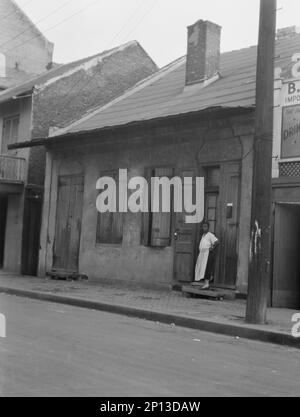 Vista dall'altra parte della strada di una donna che si trova accanto a una porta nel quartiere francese di New Orleans, tra le 1920:1926 e le 17:00. Foto Stock