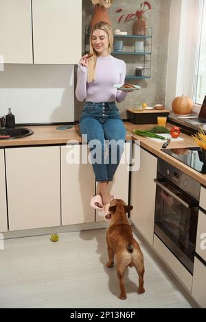 Donna compiaciuta che mangia biscotti dell'avena in presenza del suo cane Foto Stock