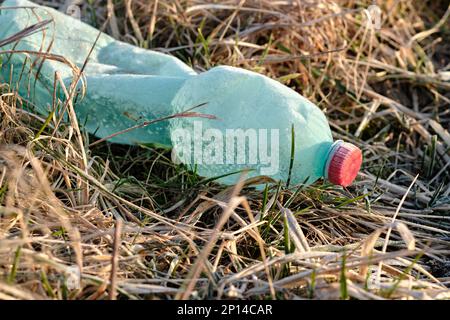 Bottiglia di plastica grattugiata coperta di ghiaccio e neve in erba secca congelata. Verde con tappo rosso del flacone. Rifiuti di plastica lasciati in natura. Foto Stock