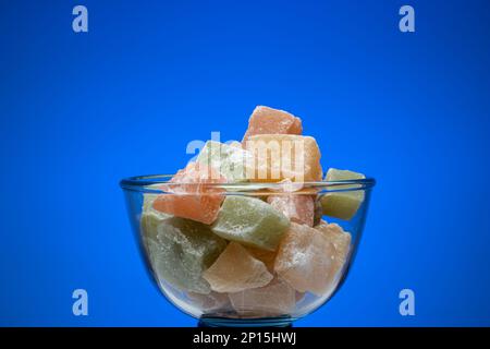 Cubetti di delizia turca colorata in una ciotola di vetro. Primo piano ripresa in studio, isolata su sfondo blu. Foto Stock