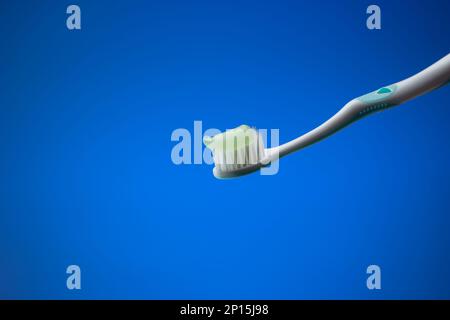Spazzolino da denti bianco in plastica con dentifricio azzurro. Primo piano ripresa in studio, isolata su sfondo blu, nessuna gente. Foto Stock