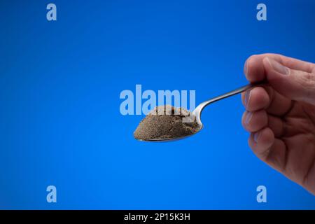 Pepe nero in polvere finemente macinato in un piccolo cucchiaio d'argento. Primo piano ripresa in studio, isolata su sfondo blu. Foto Stock