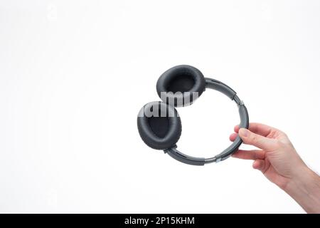Cuffie generiche wireless ad auricolare tenute in mano da una mano maschio caucasica. Primo piano ripresa in studio, isolata su sfondo bianco. Foto Stock