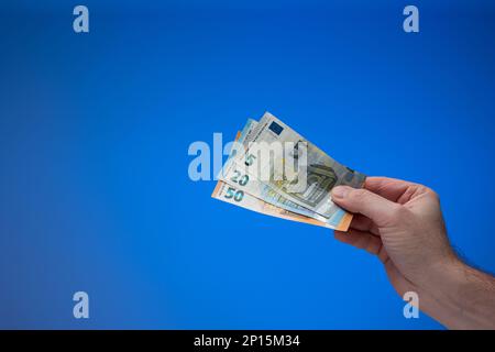 Banconote in euro in mano maschile. Primo piano ripresa in studio, isolata su sfondo blu. Foto Stock