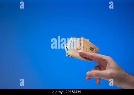 Banconote in euro in mano maschile. Primo piano ripresa in studio, isolata su sfondo blu. Foto Stock