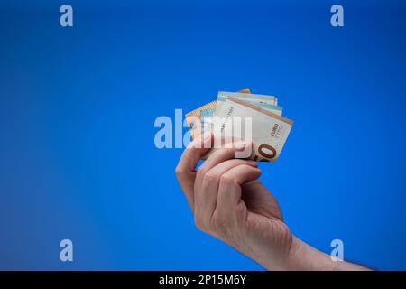 Banconote in euro in mano maschile. Primo piano ripresa in studio, isolata su sfondo blu. Foto Stock