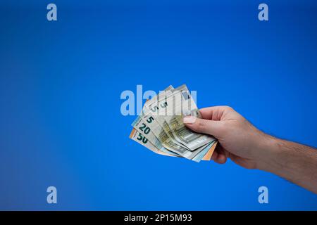 Banconote in euro in mano maschile. Primo piano ripresa in studio, isolata su sfondo blu. Foto Stock