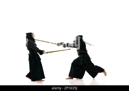 Uomini, atleti professionisti di kendo in uniforme piovendo con spada di shinai su sfondo bianco studio. Vincitore Foto Stock