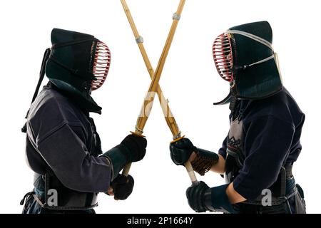 Due uomini, lottatore di kendo professionista, atleti in uniforme nera, incrociando le spade contro lo sfondo bianco dello studio Foto Stock