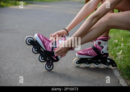 Una ragazza con unghie rosa mette su pattini del rullo. Foto Stock