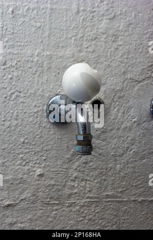 Rubinetto dell'acqua del rubinetto montato a parete con manopola rotonda bianca in lavanderia. Foto Stock