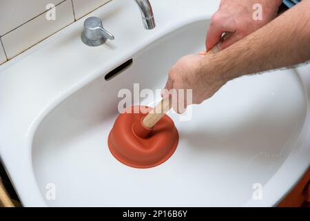 Mano maschio caucasica che tiene uno stantuffo che scollega un lavandino della stanza da bagno. Foto Stock