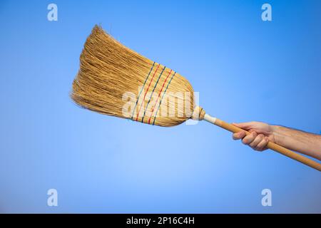Mano maschio caucasica che tiene una scopa intrecciata isolata su sfondo blu. Foto Stock