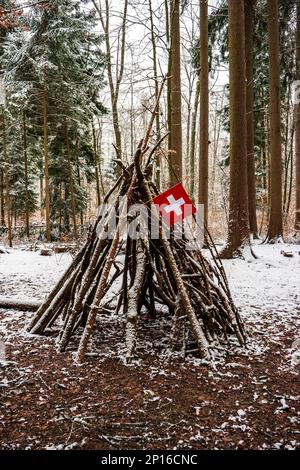 Ramo di albero fatto capanna tenda di legno gioco nella foresta battenti una piccola bandiera nazionale svizzera. Foto Stock