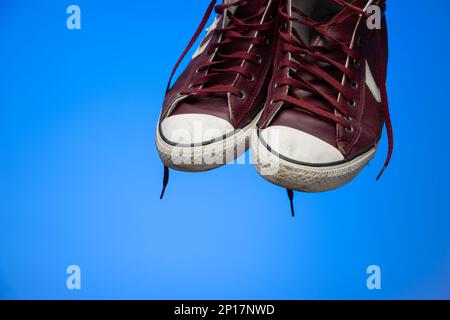 Coppia di vecchie scarpe rosse logore e sporche isolate su sfondo blu ripresa in studio. Foto Stock