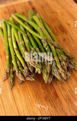 Mazzo di asparagi freschi verdi stagionali su un tavolo da cucina in legno da vicino vista dall'alto profondità di campo poco profonda. Foto Stock