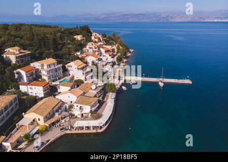 Vista aerea del drone di Kassiopi, villaggio nella costa nord-orientale dell'isola di Corfù, Isole IONIE, Kerkyra, Grecia in una giornata di sole estate, con porto turistico, città, b Foto Stock