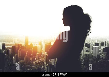 Il suo successo è stato plasmato in questa città. Un'immagine silhouetted di una giovane donna d'affari che guarda un paesaggio urbano da una finestra d'ufficio. Foto Stock