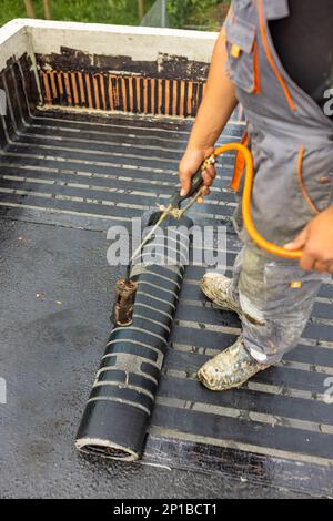 Gli operatori che collocano una barriera al vapore sul tetto utilizzando una torcia a gas propano per la saldatura di lastre di bitume. Foto Stock