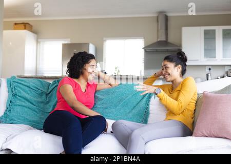 Felici amici biraciali femmina seduti sul divano e parlando Foto Stock