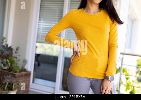 Sezione centrale di donna biraciale indossa una camicia gialla a maniche lunghe con spazio copia Foto Stock
