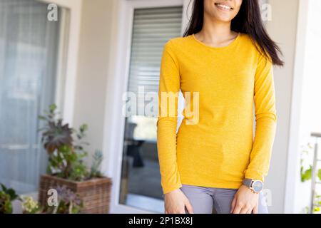 Sezione centrale di donna biraciale indossa una camicia gialla a maniche lunghe con spazio copia Foto Stock