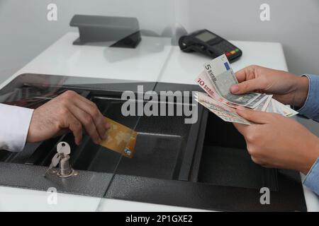 Donna che mette denaro sulla carta in banca, primo piano. Cambio valuta Foto Stock