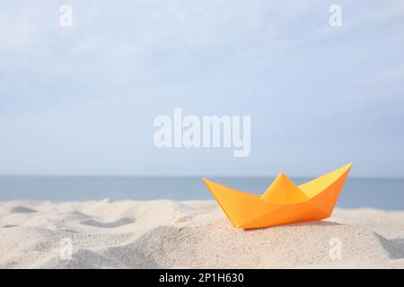 Barca di carta arancione sulla spiaggia sabbiosa vicino al mare, spazio per il testo Foto Stock