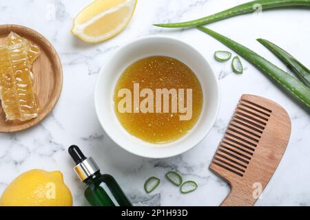 Maschera fatta in casa in ciotola, ingredienti e pettine di bambù su tavolo di marmo bianco, piatto Foto Stock