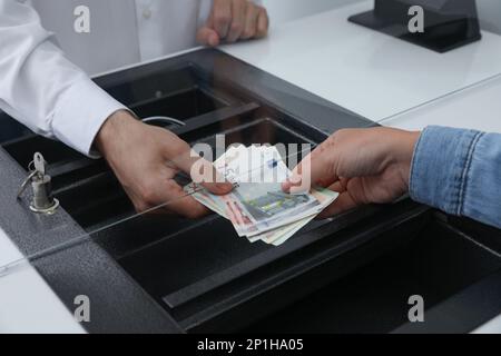 Donna che dà denaro al cassiere in banca, primo piano. Cambio valuta Foto Stock