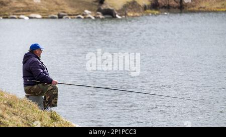 Minsk, Bielorussia - 11 aprile 2022: Pescatore con una canna da pesca sulla riva del lago. Pesca primaverile Foto Stock