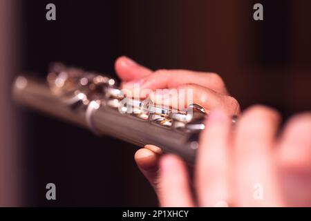 Un ritratto delle dita di una mano di un musicista flautista che stringe le valvole di un flauto metallico d'argento per suonare una nota di un brano musicale durante Foto Stock