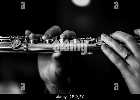 Ritratto in bianco e nero delle dita di una mano di un musicista flautista che stringe le valvole di un flauto metallico d'argento per suonare una nota Foto Stock