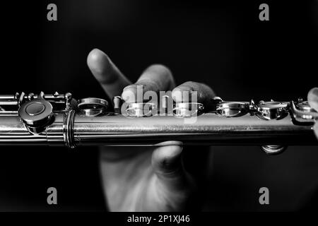 Un ritratto in bianco e nero delle dita di una mano di un musicista flautista che preme sulle valvole di un flauto d'argento metallico per suonare una nota di un musi Foto Stock