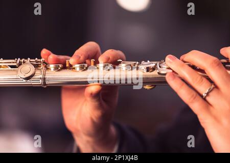 Un ritratto ravvicinato delle dita di una mano di un musicista flautista che stringe le valvole di un flauto di metallo d'argento per suonare una nota di una torta musicale Foto Stock