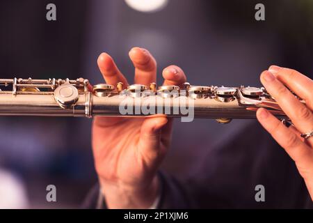 Un ritratto ravvicinato delle dita di una mano di un musicista flautista che stringe le valvole di un flauto d'argento metallico per suonare una nota di una torta musicale Foto Stock