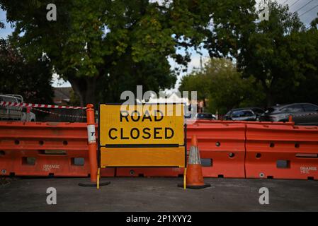 Cartello giallo chiuso di fronte alle barriere arancioni in una verde strada suburbana di Melbourne Foto Stock