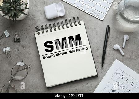 Notebook con testo SMM (Social Media Marketing) e altri oggetti su tavolo grigio, piano Foto Stock