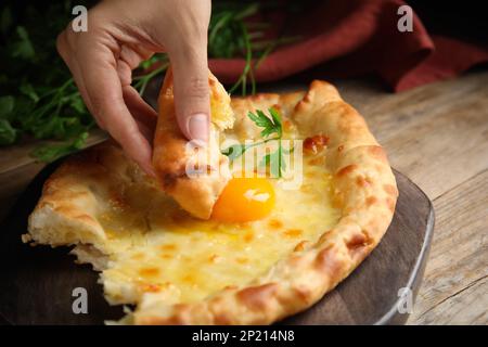 Donna che mangia delizioso Khachapuri Adjarian al tavolo di legno, primo piano Foto Stock