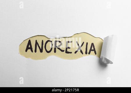 Anoressia parola scritta su sfondo beige, vista attraverso il foro in carta bianca Foto Stock